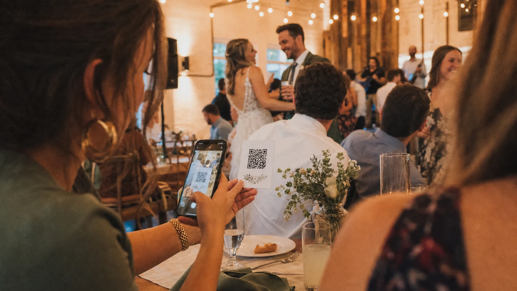 A wedding guest scanning a QR code while the couple celebrates at the reception.